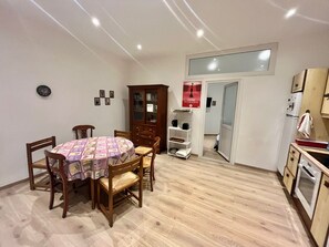 A compact kitchen with wooden cabinets, a dining table with chairs, and a small refrigerator. - woody (Cannes)
