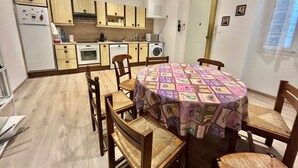 A compact kitchen with wooden cabinets, a dining table with a patterned tablecloth, and a washing machine. - woody (Cannes)