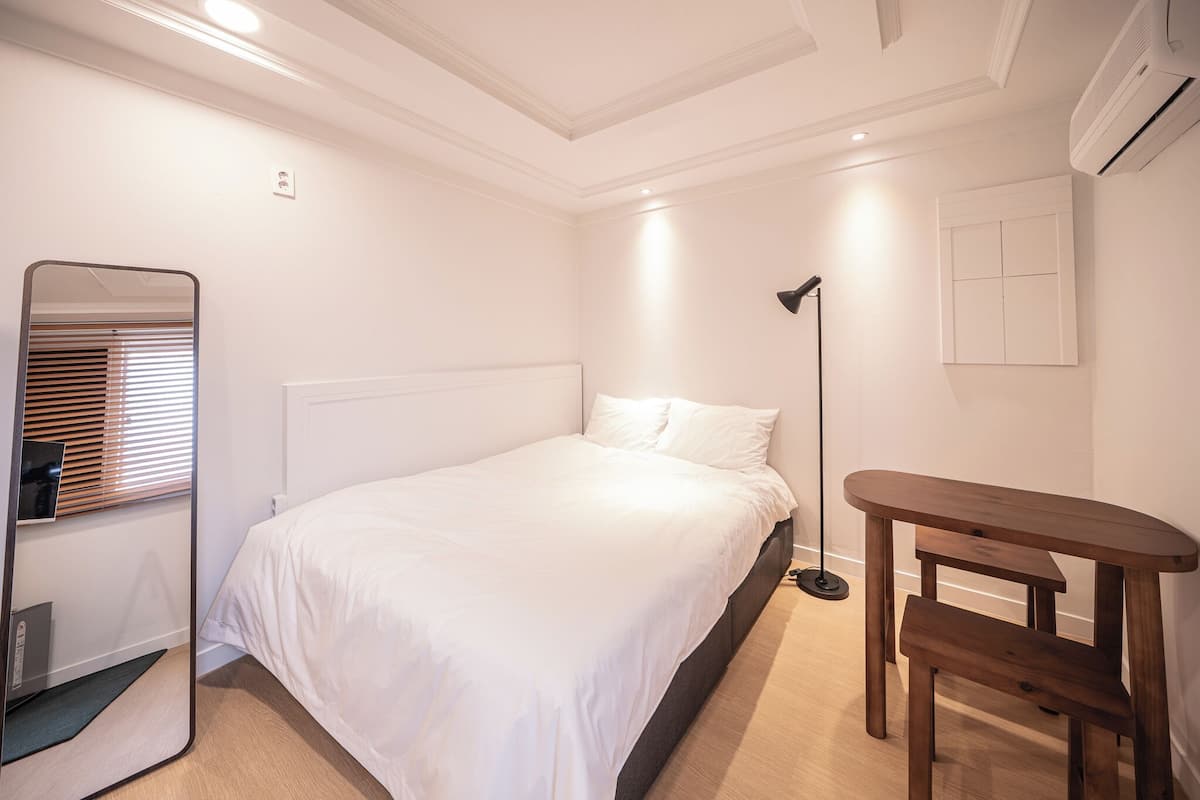 Ein Schlafzimmer mit einem Bett, einem Nachttisch, einem Spiegel und einer Stehlampe.