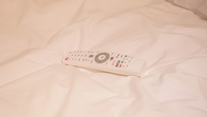 Une télécommande posée sur un lit aux draps blancs.