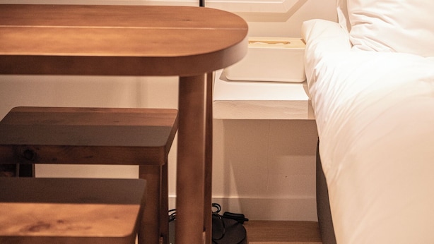 Une chambre d’hôtel bien rangée, avec une table en bois, un lampadaire noir et un lit blanc.