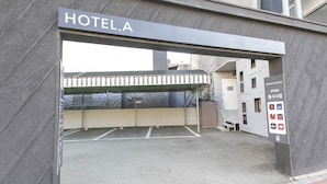 L’entrée d’un hôtel, avec une enseigne indiquant « HÔTEL A » et un panneau de signalisation pour le stationnement au-dessus.