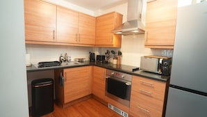 A compact kitchen with wooden cabinets, a built-in oven, a toaster, and a trash bin.