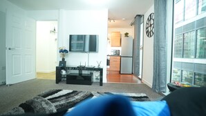 A modern living room with a flat-screen TV, a black coffee table, and a large window with curtains.