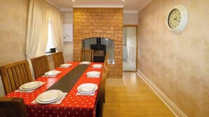 A dining area with a long table set for a meal, a stone fireplace, and a clock on the wall.