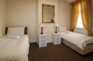 A hotel room with two beds, a mirror, two bedside tables with lamps, and a window with curtains.