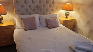 A neatly made bed with a tufted headboard, two bedside tables with lamps, and a patterned wallpaper.