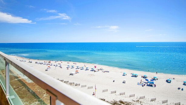 A beach with umbrellas and people, a clear sky, and a view of the ocean. - Cozy Pet Friendly Beachfront Retreat On Top Floor (Orange Beach)