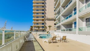 A poolside area with lounge chairs and a pool, surrounded by a high-rise building with balconies. - Cozy Pet Friendly Beachfront Retreat On Top Floor (Orange Beach)