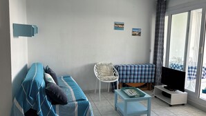 Een woonkamer met een bank, een bijzettafeltje, een stoel, een tv op een dressoir en een raam met uitzicht.