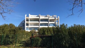 Een meerhoog gebouw met balkons, omgeven door groen en een helderblauwe lucht.