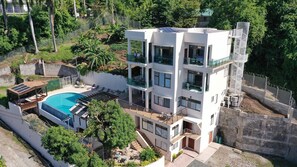 A modern multi-story building with a swimming pool, outdoor seating, and a view of surrounding greenery. - Yellow Sands Luxury Villas Unit 1 (Castries)