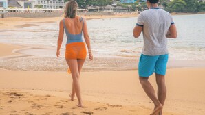 A beach with two people walking, a sandy shore, and buildings in the background. - Yellow Sands Luxury Villas Unit 1 (Castries)