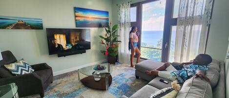 A living room with a large flat-screen TV, a sofa, a coffee table, and a potted plant.