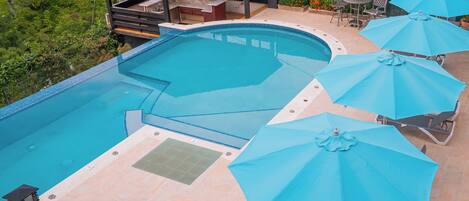 A swimming pool with a hot tub, outdoor seating, and umbrellas.