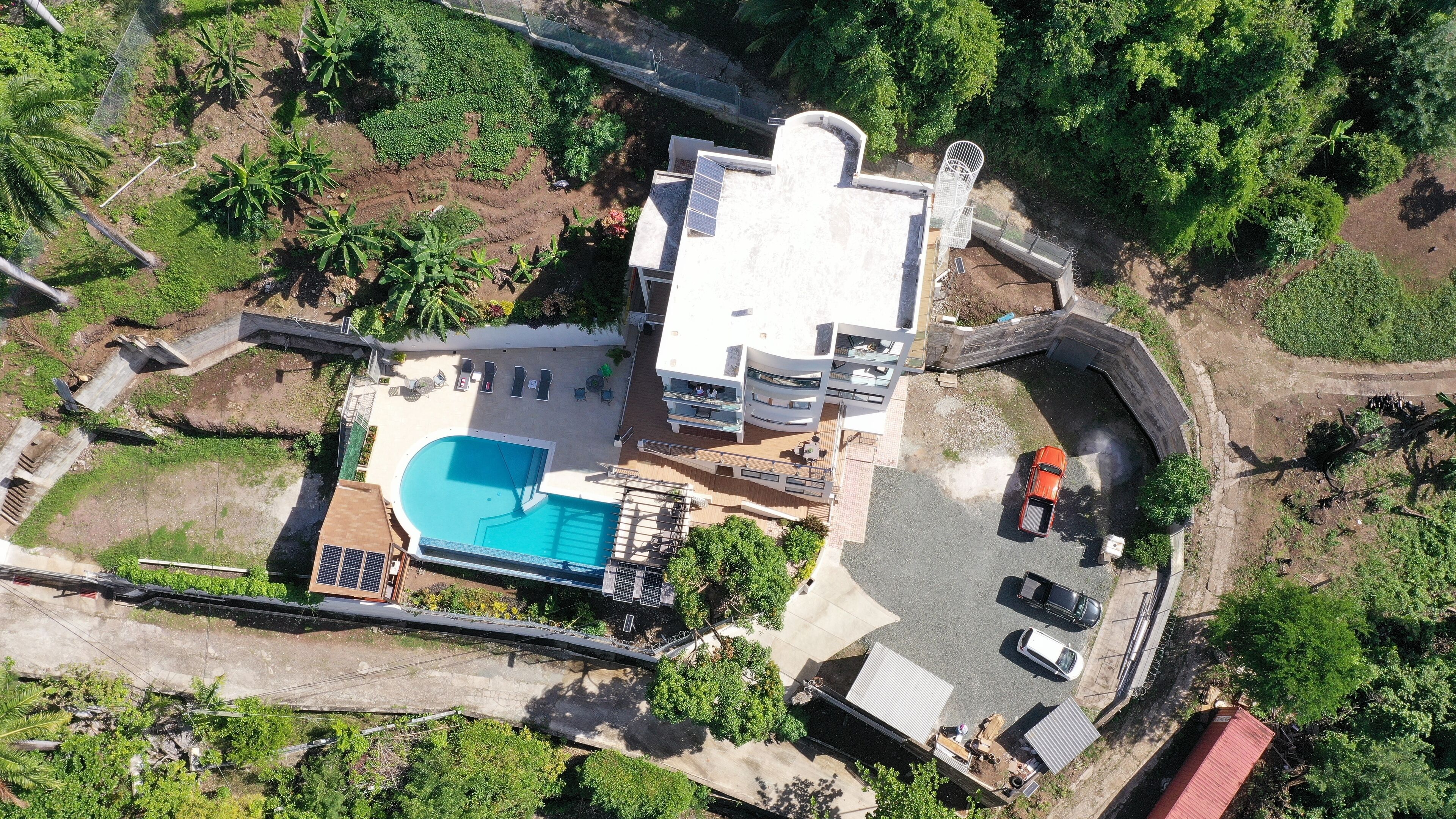 An aerial view of a modern house with a swimming pool, solar panels, and a curved driveway.