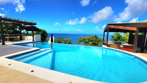 A clear blue pool with a view of the ocean, surrounded by outdoor seating and a covered area. - Yellow Sands Luxury Villas Unit 1 (Castries)