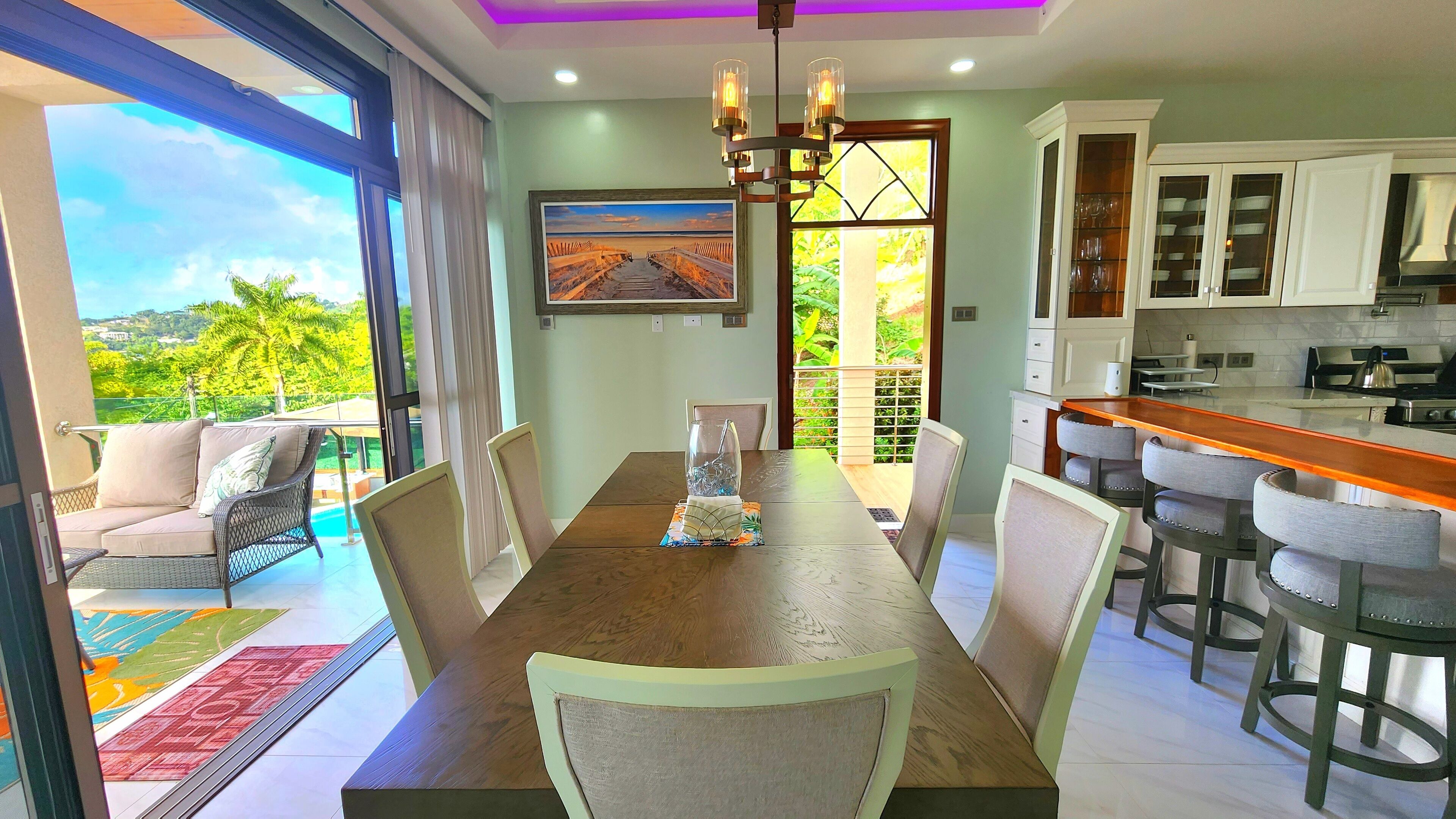 A dining area with a view of a balcony, a kitchen with white cabinets, and a chandelier.