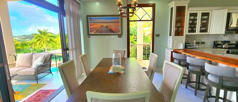 A dining area with a view of a balcony, a kitchen with white cabinets, and a chandelier.