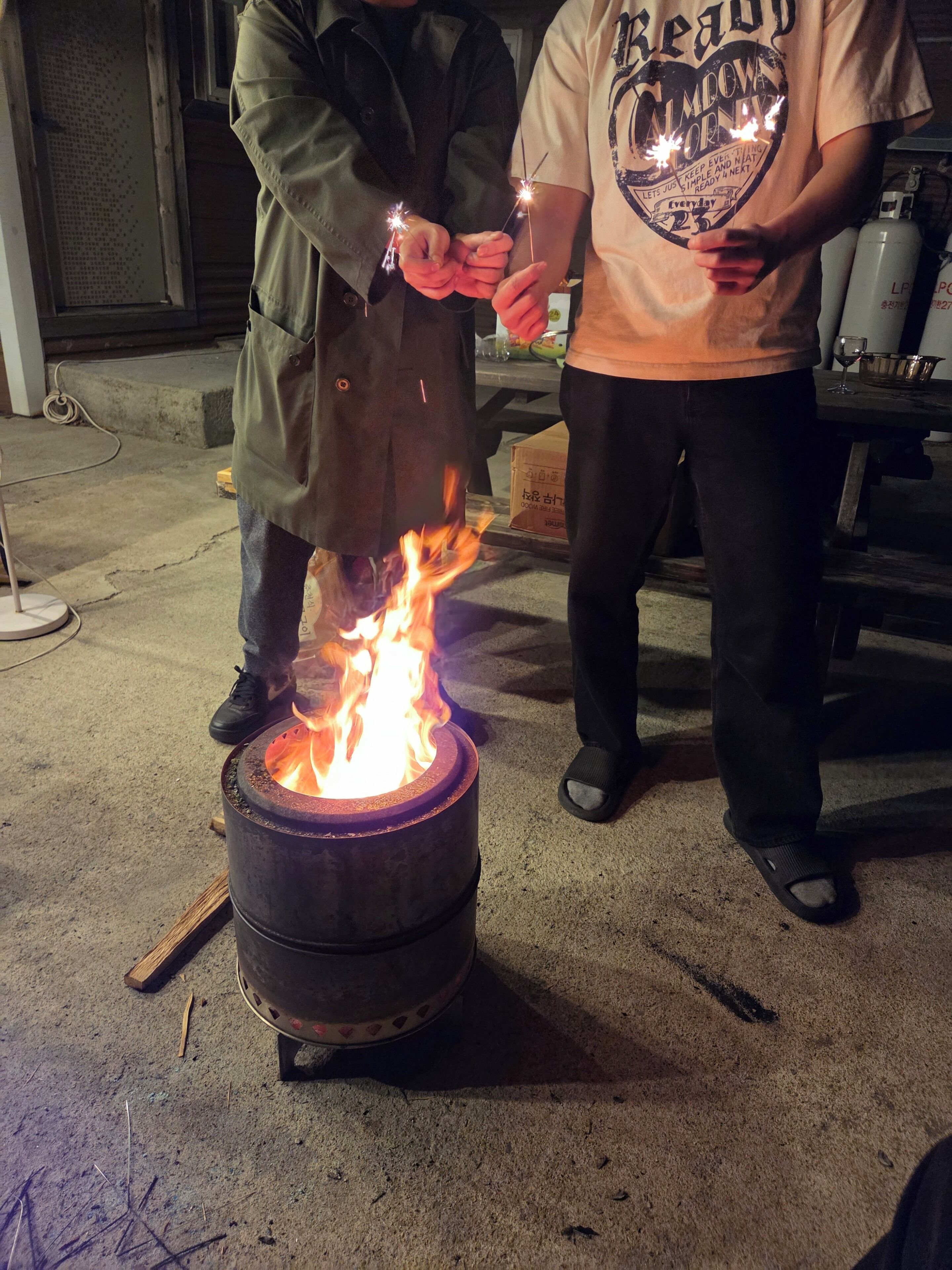 Dos personas sosteniendo bengalas cerca de un fuego en un barril.
