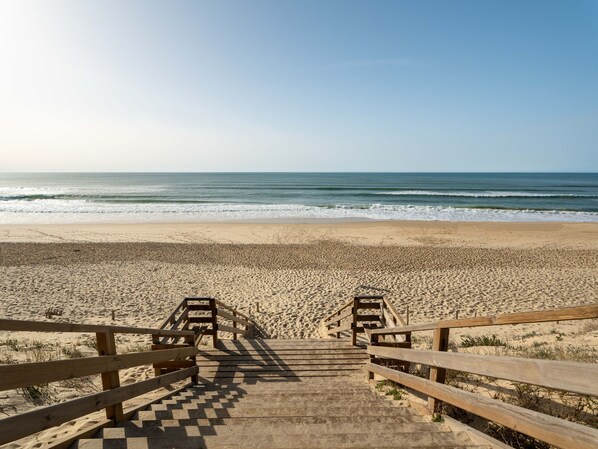 Eine Holztreppe führt zu einem Sandstrand mit Blick auf den Ozean.