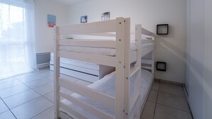 Una cama literera en una habitación con paredes blancas, una lámpara en el techo y una ventana con cortinas.