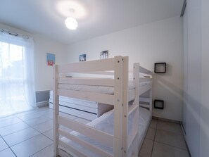 Un letto a castello in una stanza con pareti bianche, una luce al soffitto e una finestra con tende.