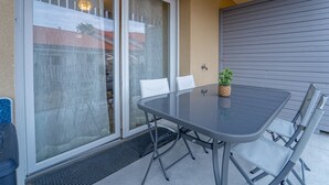 Una mesa con superficie de vidrio, cuatro sillas, una planta en maceta y un ventanal corredero que da a un espacio exterior cubierto.