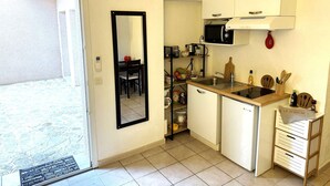 A compact kitchen with a microwave, sink, and small refrigerator. A mirror is mounted on the wall, and there is a door leading outside.