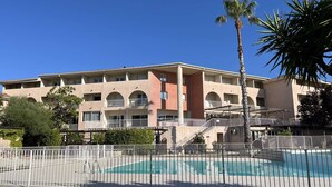 A multi-story hotel with a swimming pool, balconies, and palm trees.
