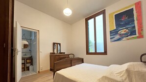 Ein Schlafzimmer mit Bett, Kommode, Spiegel, Fenster und einer Tür zu einem Badezimmer.