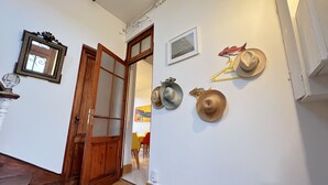 Ein Flur mit Holzboden, einer Holztür und einer weißen Wand mit einem gerahmten Bild und mehreren Hüten, die an der Wand hängen.