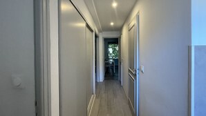 Un couloir étroit avec un plancher en bois, des murs blancs et une porte au fond.