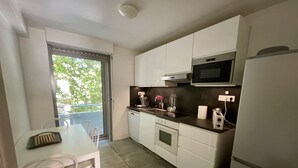 Une cuisine compacte avec des meubles blancs, un four à micro-ondes, un grille-pain et un lave-vaisselle. On y trouve une table à manger avec des chaises et une fenêtre donnant sur un espace verdoyant.