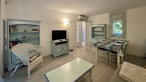 Un salon comprenant un téléviseur, un canapé blanc, une table à manger avec des chaises et une bibliothèque.
