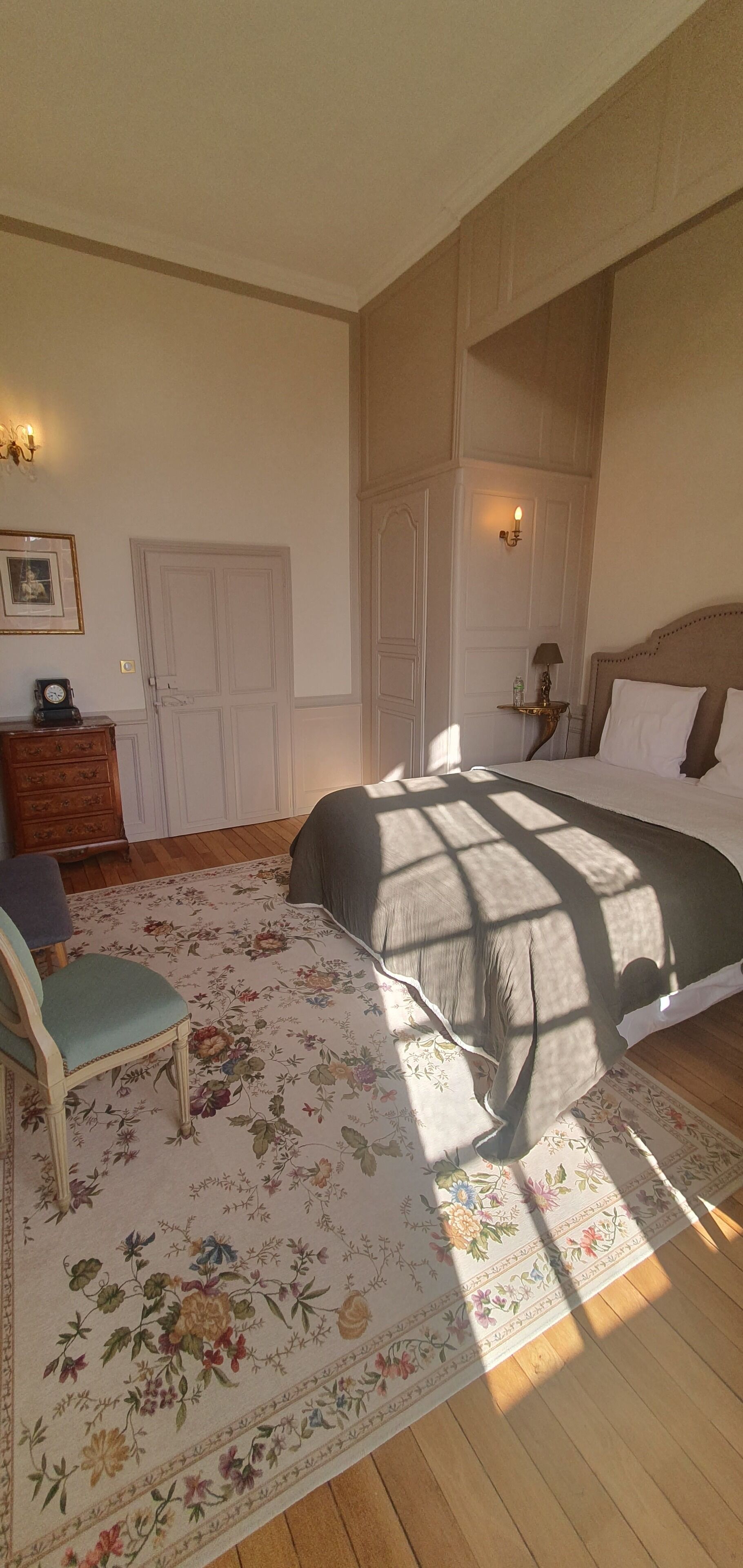 Une chambre à coucher avec un grand lit, une chaise, une commode et une porte.