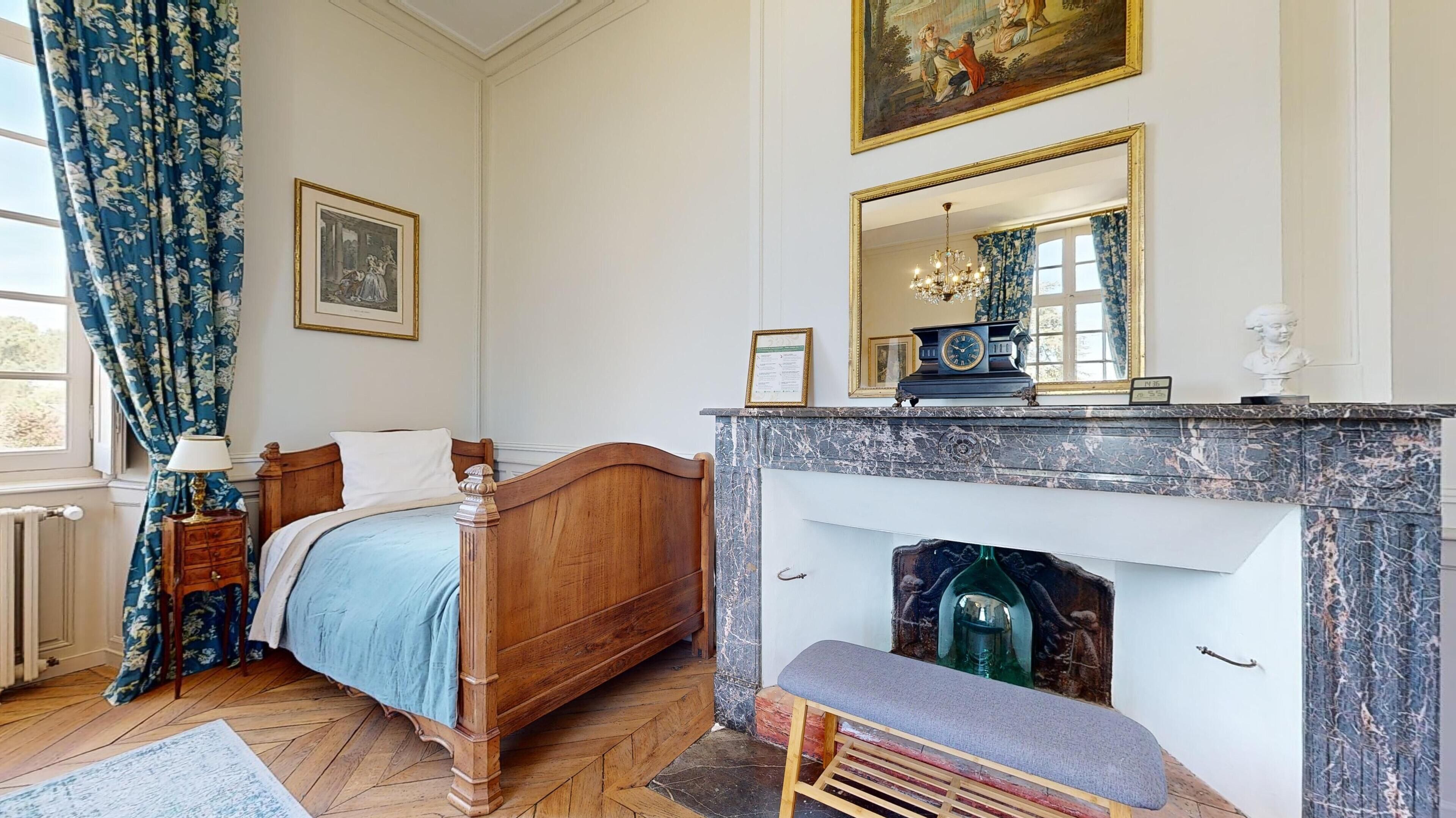 A bedroom with a wooden bed, a marble fireplace, a chandelier, and a large mirror above the fireplace.