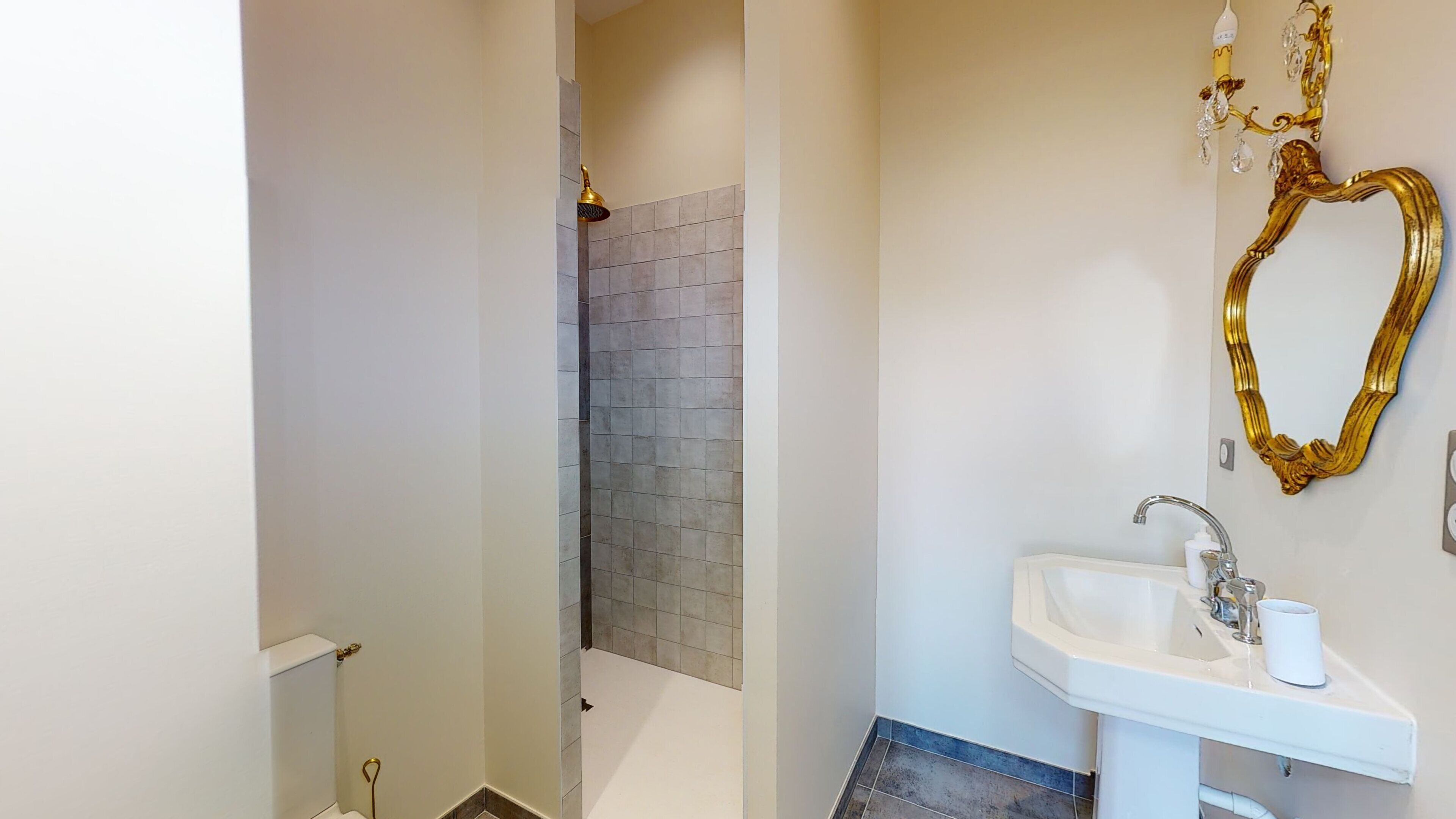 A bathroom with a white sink, a gold mirror, and a shower area with grey tiles.