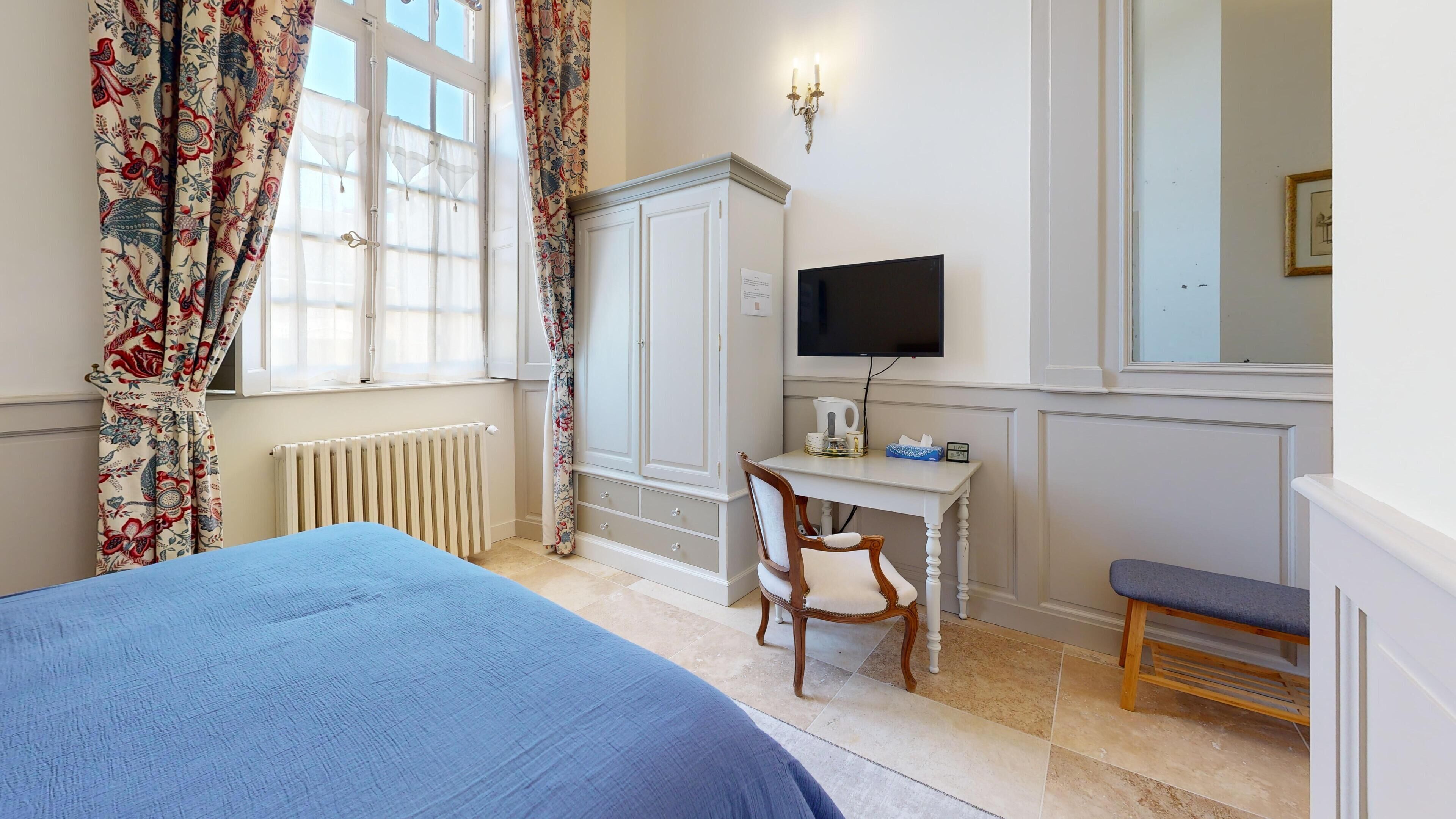 Un dormitorio con una cama, un escritorio con una silla, un televisor y un radiador.