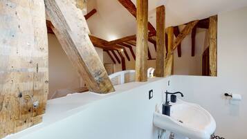 Een rustieke badkamer met zichtbare houten balken, een wit wastafelmeubel en een witte badkuip.