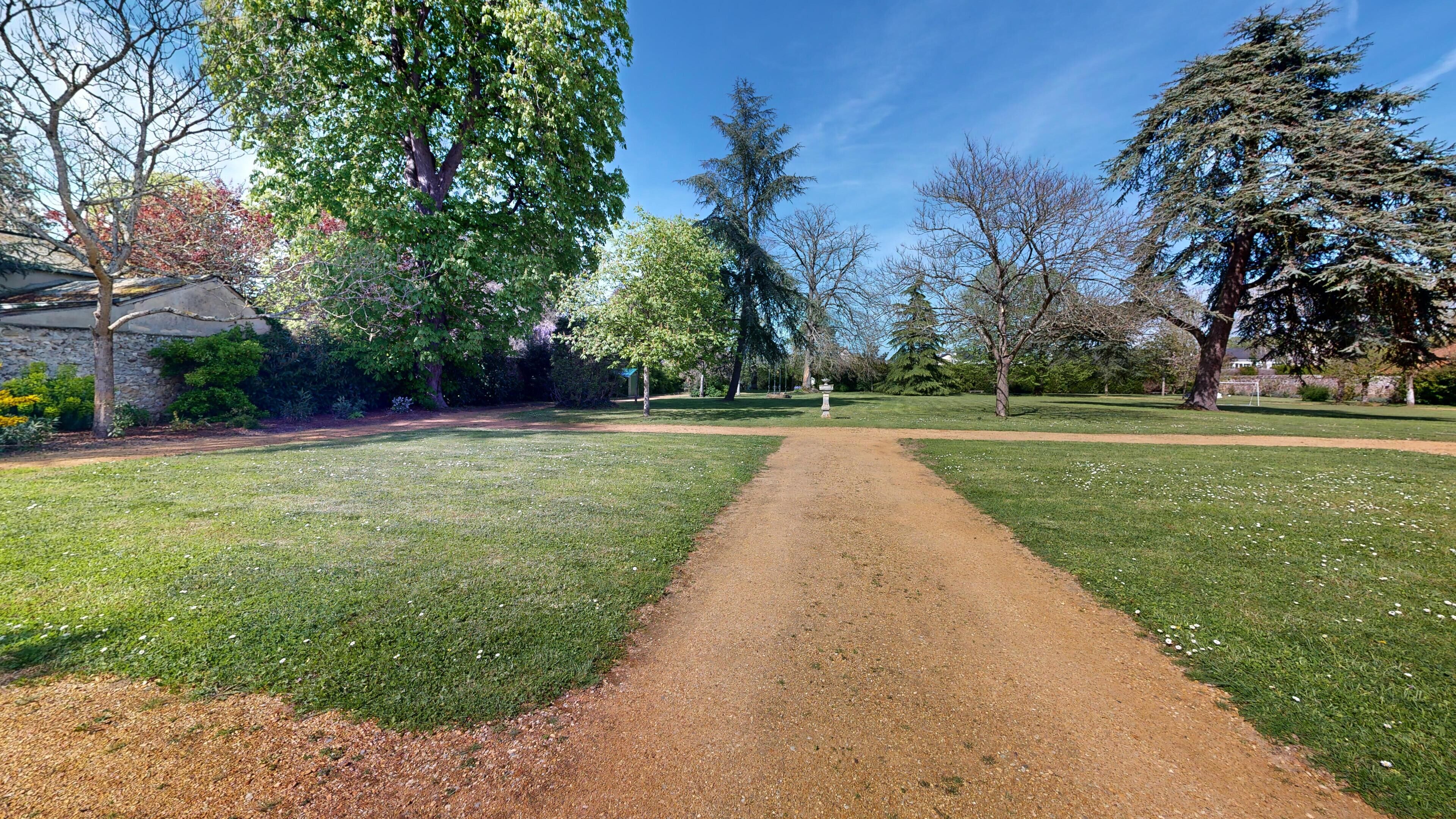 A well-maintained grassy area with a gravel path leading through it, surrounded by trees and a stone wall.