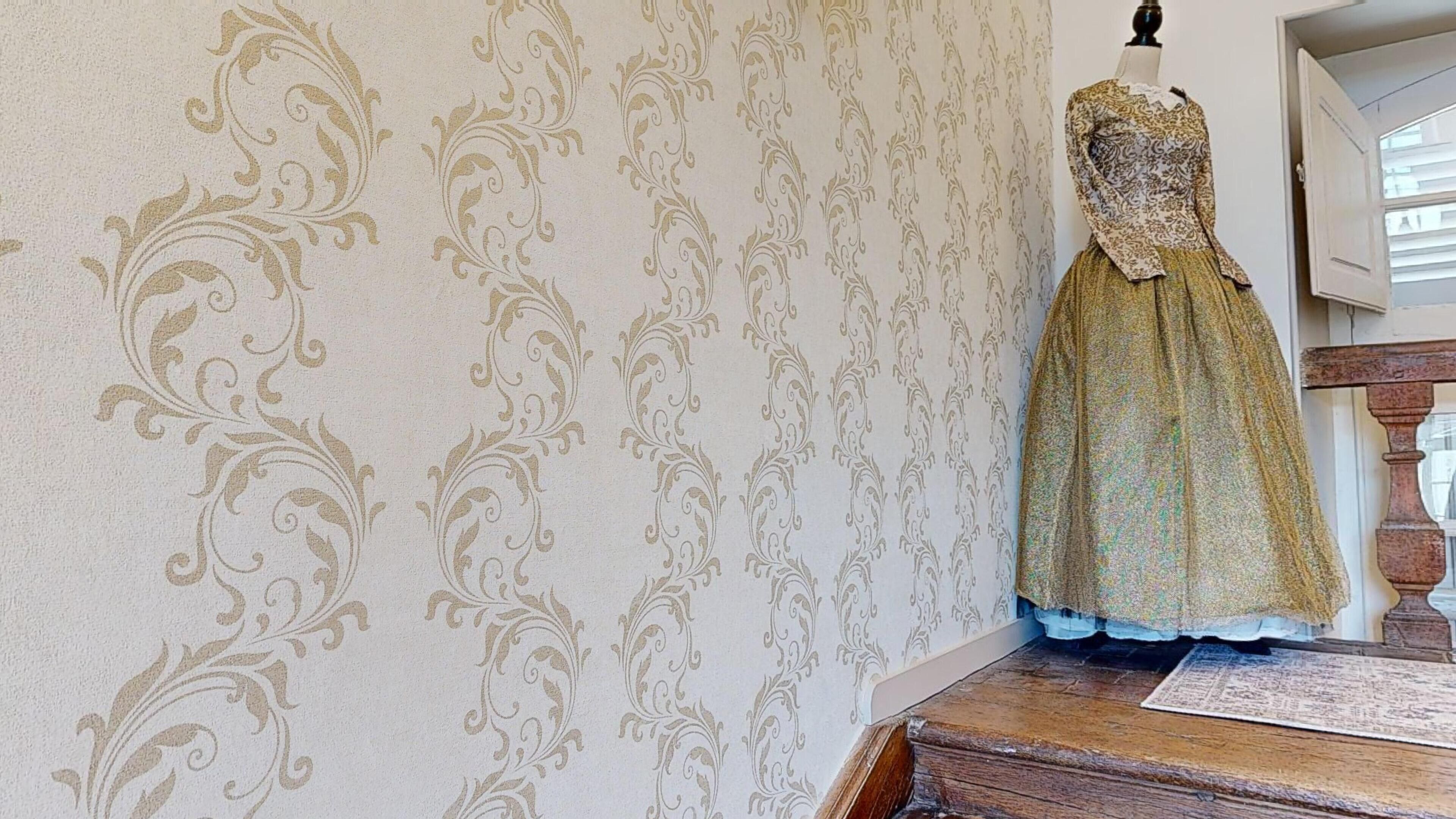 A mannequin in a dress against a wallpaper with a floral pattern.