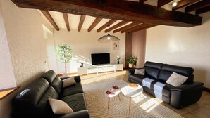 Een woonkamer met een zwarte leren bank, een witte salontafel en een televisie op de achtergrond.