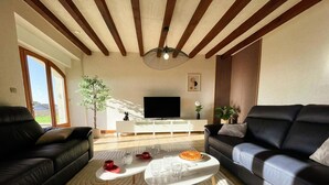 Een moderne woonkamer met een grote televisie, twee zwarte banken, een salontafel en een groot raam met uitzicht.