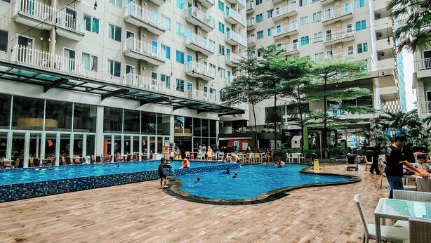 A swimming pool area with wooden decking, surrounded by high-rise residential buildings. - Bogor Icon Condotel by Holla (Bogor)