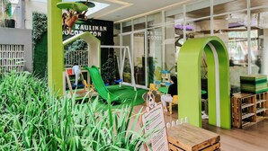 A modern indoor play area with a green slide, climbing structures, and a playhouse. - Bogor Icon Condotel by Holla (Bogor)