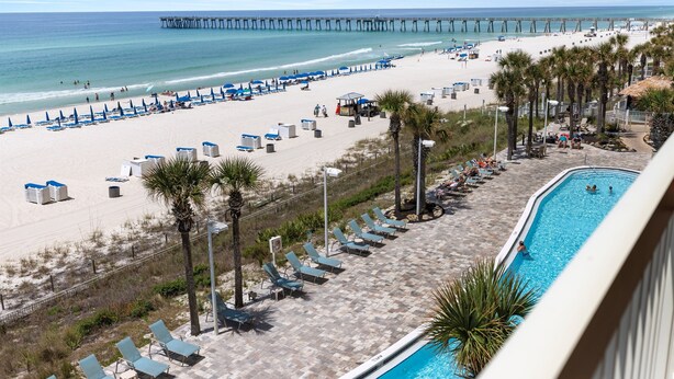A beach resort with a swimming pool, lounge chairs, and a pier in the background.