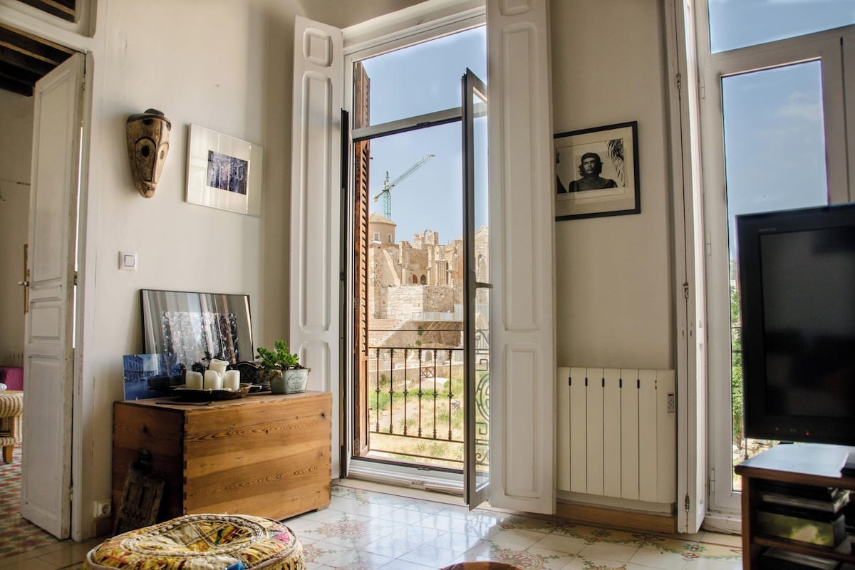 A spacious living room with a large window, a wooden cabinet, and a television.