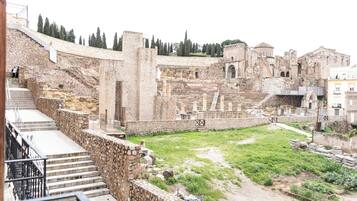 An ancient amphitheater with stone steps leading up to the seating area, surrounded by modern buildings.