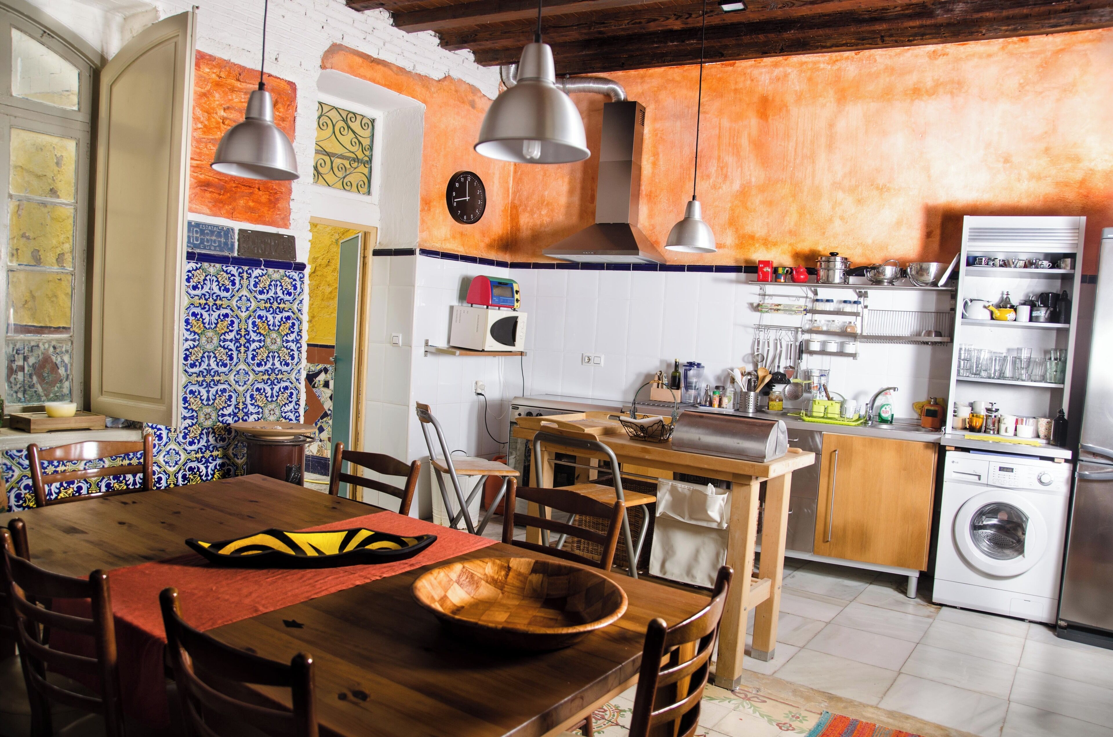 A kitchen with a wooden table, chairs, a washing machine, and a microwave.